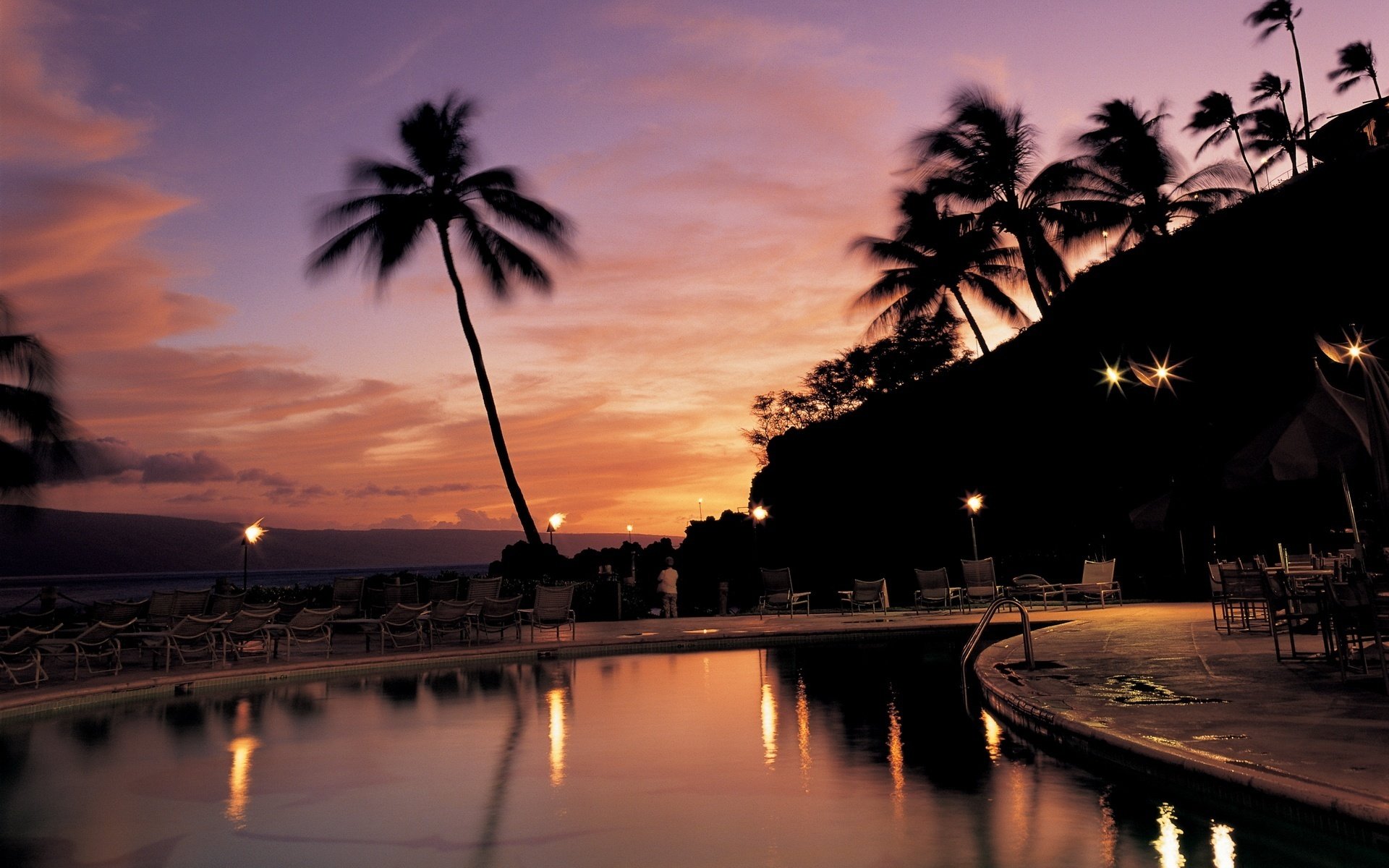 superficie dell acqua sera lanterne lettini piscina tramonto palme cielo relax hotel resort sedie a sdraio sagome crepuscolo alberi tropici cielo rosa luci riflessione